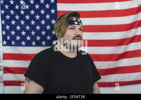 Bärtiger Kaukasier, der ein Bandana trägt, während er davor steht Der US-Flagge Stockfoto