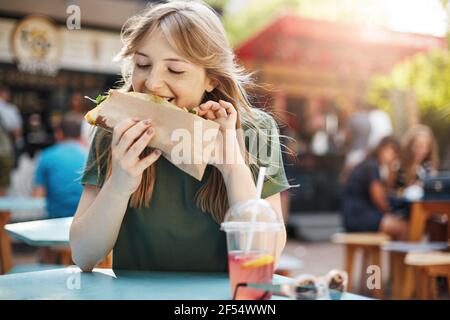 Mädchen essen Taco. Hungrige Sommersprossen blonde Frau essen Junk-Food auf einem Food Court an einem sonnigen Sommertag im Park. Stockfoto