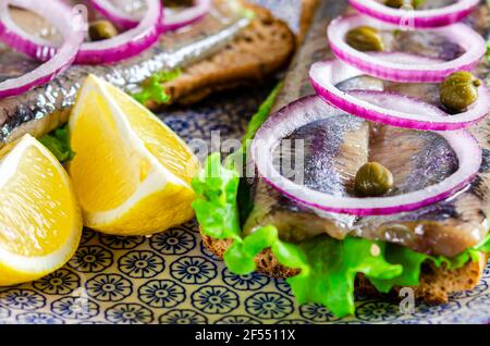 Appetitliches Smorrebrod mit norwegischem Hering, Salat, blauer Zwiebel, Zitrone und Tomate liegt auf einem Holzbrett Stockfoto