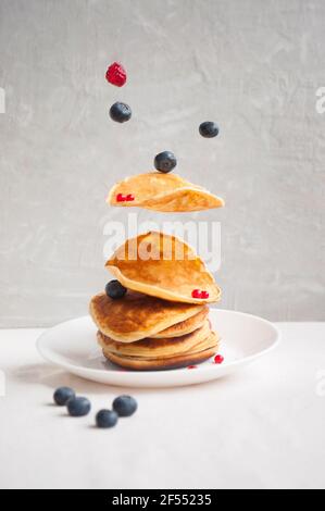 Fliegende frisch gekochte Pfannkuchen und Beeren mit Honig, Walnuss zum Frühstück. Stockfoto