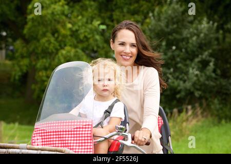 Porträt einer jungen Mutter, die ihre Tochter mit dem Fahrrad fährt Im Park Stockfoto
