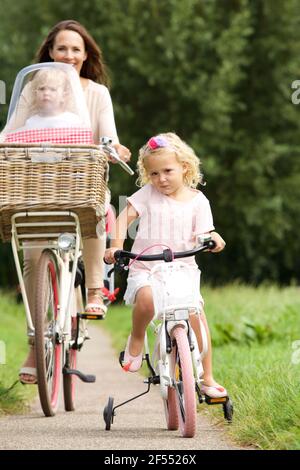 Porträt einer jungen Frau mit zwei kleinen Mädchen auf Fahrrädern Im Park Stockfoto