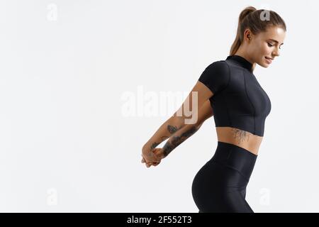 Fitness trainierte weibliche Stretching Arme hinter dem Rücken, dabei Aufwärmübungen. Läuferin mit feinem Körper trainieren vor dem Joggen in Sportswear, weiß Stockfoto