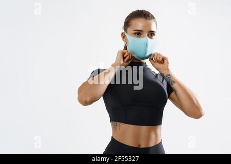 Portrait von fit Frau setzen auf eine schützende Gesichtsmaske und Training. Sportliche Sportlerin trägt Gesichtsmaske in der Turnhalle während Coronavirus Ausbruch, weiß Stockfoto