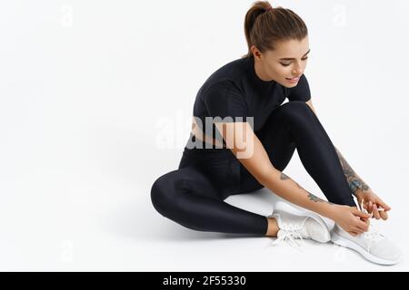 Fitness Frau in Sportbekleidung sitzt auf dem Boden vor dem Training. Weibliche Athletin, die Schnürsenkel bindet, macht sich bereit für das Training. Mädchen im aktiven Ohr Stockfoto