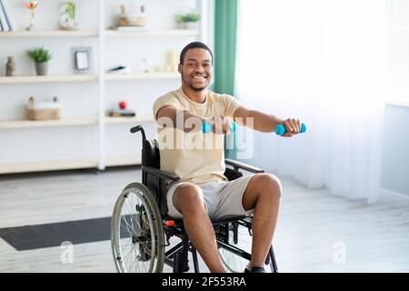 Rehabilitation von behinderten Menschen. Junger afroamerikanischer Mann im Rollstuhl, der zu Hause arbeitet Stockfoto