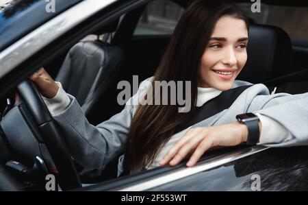 Elegante und selbstbewusste Geschäftsfrau, die aus dem Autofenster schaut, bei der Arbeit fährt und Sicherheitsgurte trägt. Frau und Fahrer mit Blick nach draußen Stockfoto