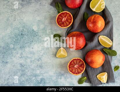 Ganze und in Halbblut sizilianischen Orangen, Limetten und Minze auf blauem Beton Hintergrund geschnitten. Draufsicht. Selektiver Fokus. Stockfoto