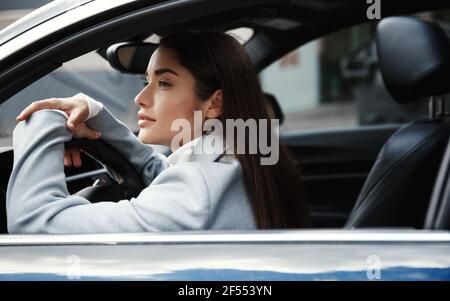 Elegante Geschäftsfrau sitzt in ihrem Auto und wartet auf jemanden, Blick auf die Stadt Straße. Die Fahrerin schaute nachdenklich aus dem Fenster Stockfoto