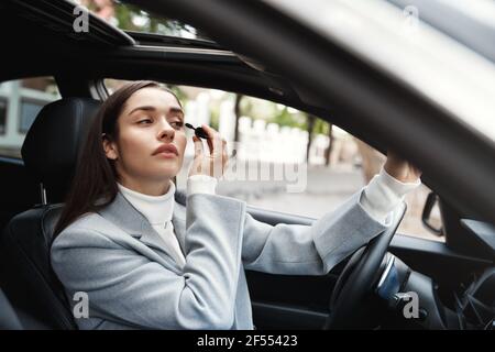 Junge schöne Frau im Auto sitzen, fahren auf Treffen und Anwendung Mascara, Blick auf Rückspiegel Stockfoto