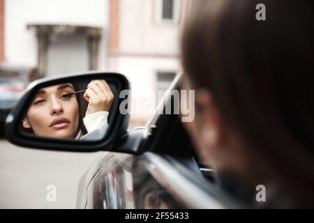 Geschäftsfrau Fahrer Blick auf Rückspiegel, während im Auto sitzen Und Wimperntusche auftragen Stockfoto