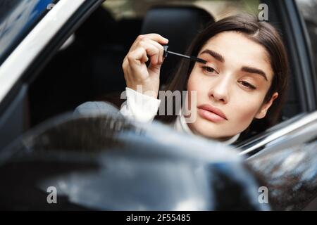 Geschäftsfrau Anwendung Mascara und Blick auf Rückspiegel, legte auf Make-up auf ihrem Weg zum Business-Meeting. Frau sitzt im Auto und Befestigung Make-up Stockfoto