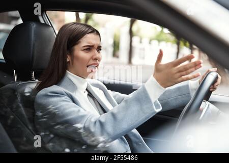 Verärgerte Geschäftsfrau steckte im Verkehr auf ihrem Weg. Verärgerte weibliche Führungskraft beschwert sich während des Autofahrens, schimpft einen anderen Fahrer Stockfoto