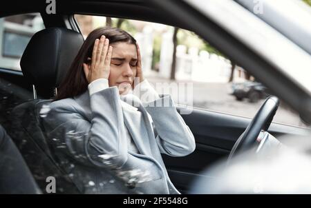 Frau mit einem Panikangriff im Auto. Geschäftsfrau, die frustriert aussieht, auf dem Fahrersitz sitzt und die Hände am Kopf hält. Autounfall und Versicherung Stockfoto