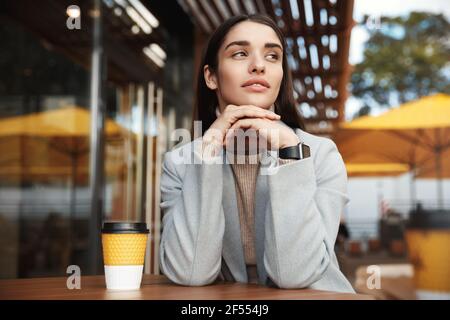 Junge Frau, die sich im Café im Freien entspannt. Geschäftsfrau wartet im Café, schaut auf der Straße nachdenklich Stockfoto