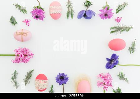Esterrahmen aus bunten Eiern, Frühlingsblumen und Lavendelblättern auf weißem Hintergrund. Flach liegend, Draufsicht Stockfoto