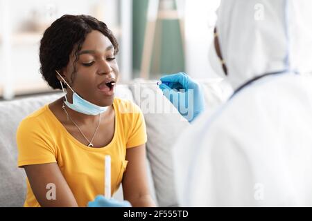 Arzt in Schutzanzug nimmt Tupfer zum Patienten, nach Hause innen Stockfoto