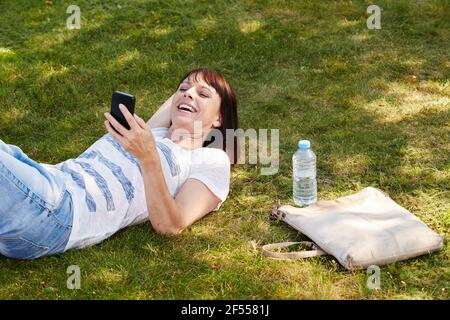 Portrait der schönen Frau im Gras liegen lächelnd mit smart Telefon Stockfoto