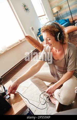 Porträt einer lächelnden Frau, die Kopfhörer in das Soundsystem einsteckt Stockfoto