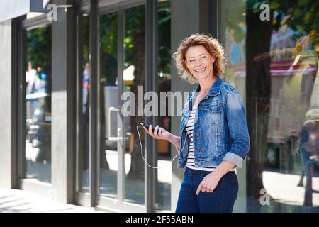 Porträt einer fröhlichen älteren Frau, die mit dem Handy in Stadt Stockfoto