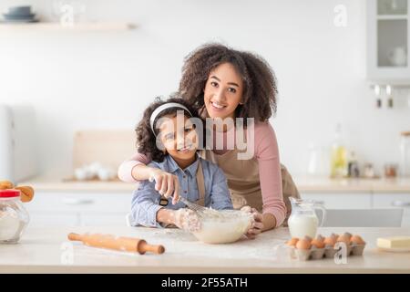 Positive schwarze Frau und Tochter Knetteig in der modernen Küche Stockfoto