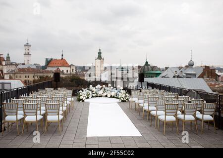 Ein wunderbarer Ort in den Dekorationen und Blumen für die Hochzeitszeremonie mit weißen Stühlen auf dem Dach des Hotels. Hochzeitszeremonie Stockfoto