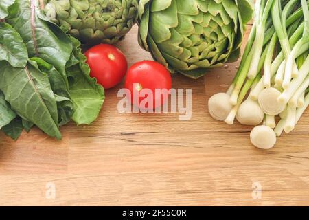 Selektiver Fokus der Vielfalt rohes grünes Gemüse Salate, grüne Artischocke, wirsing-Kohl, grüne Zwiebel und Kirschtomaten als Rahmen über Holzstruktur. Stockfoto