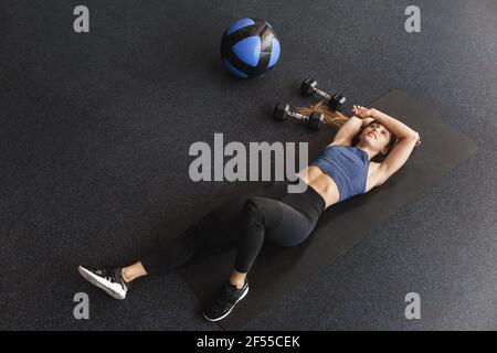 Mädchen erreicht heutigen Ziel in der Turnhalle. High-Angle-Ansicht Sportlerin Gefühl angenehme Müdigkeit nach dem Training, liegend auf Gummi-Matte im Fitnesscenter in der Nähe Stockfoto