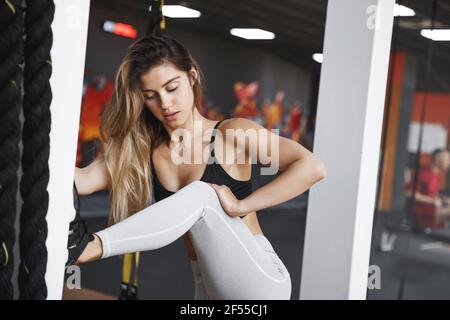 Frau in der Mitte des Aufwärm-Training im Fitnessstudio, heben Sie Bein auf Säule Stretching vor dem sportlichen Training im Fitness-Health-Club, schauen konzentriert und Stockfoto