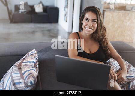 Charmante junge Unternehmerin sitzt bequem Co-Working Couch Turn beiseite Frage beantworten sprechender Kunde steht in der Nähe lächelnd niedlich Stockfoto
