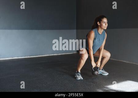 Noch ein Sit-up, um das Ziel zu erreichen. Gut aussehende motivierte hispanic Sportlerin tragen activewear, Look entschlossen halten kettlebell, machen Fitness crossfit Stockfoto