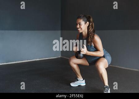 Mädchen bereiten Körper gute Form, führen aktiven Lebensstil, bestimmt gewinnen starke Muskeln, Sportlerin durchführen Kniebeugen Übung, heben kettlebell lächeln Stockfoto