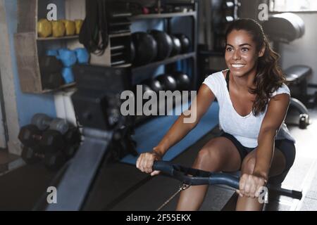 Produktives Fitness-Workout, aktives Lifestyle-Konzept. Glückliche, motivierte junge Sportlerin, lächelnd wie die Kontrolle der eigenen Grenzen im Fitnessstudio, mit Bein Stockfoto