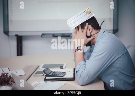 Ein Geschäftsmann, der Schutzmasken trägt und Dokumente hält, fühlt sich im Tagungsraum müde und besorgt. Stockfoto
