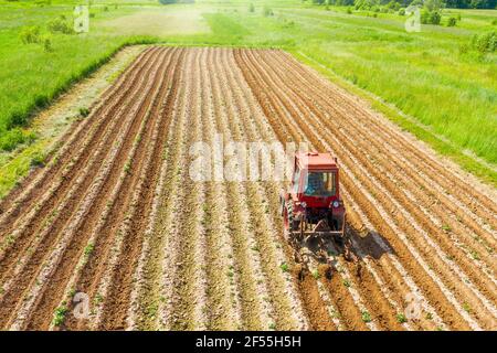 Spudding Boden in der Nähe Reihe Feld Gemüsepflanzen mit einem Traktor und Landmaschinen, Luftbild ländliche Landschaft Rückansicht Stockfoto