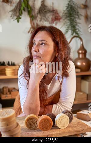 Nachdenkliche Frau mit Bio-Seifen auf Holzbrett in der Werkstatt Stockfoto