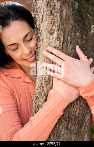 Liebevolle Frau umarmt Baumstamm im Garten Stockfoto