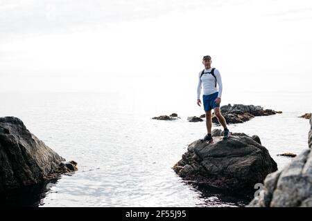 Reifer Mann, der auf Felsen inmitten des Meeres gegen den klaren Himmel steht Stockfoto