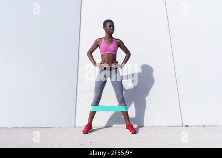 Fit junge Frau mit Gummiband tun Bein-Übung, während An einer weißen Wand stehend Stockfoto