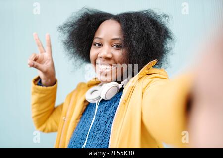 Junge Frau tut Friedenszeichen gegen Wand Stockfoto