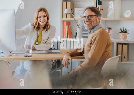 Ärztin und Patientin lächeln, während sie in der Arztpraxis sitzen Stockfoto