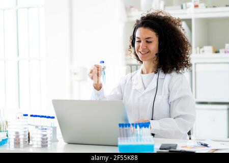 Lächelnde Forscherin mit Reagenzglas, das am Laptop arbeitet Klinik Stockfoto