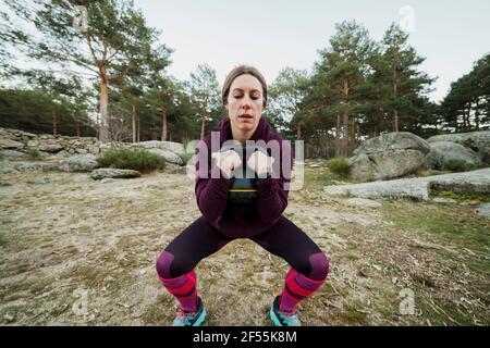 Frau mit mittlerem Erwachsenen in Hockstellung, die beim Halten trainiert kettlebell im Wald Stockfoto