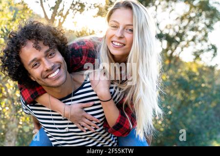Verspielte Frau Huckepack auf Mann lächelnd, während vor stehen Oder Hinterhof Stockfoto