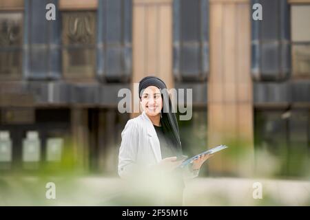 Lächelnde arabische Geschäftsfrau schaut weg, während sie draußen steht Stockfoto