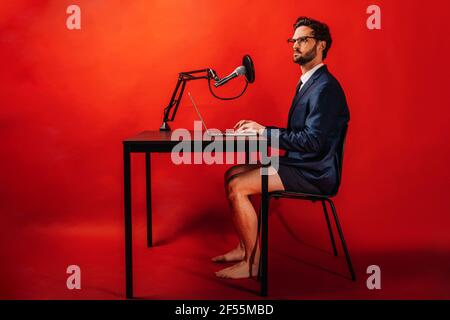 Geschäftsmann mit Laptop am Schreibtisch mit rotem Hintergrund Stockfoto
