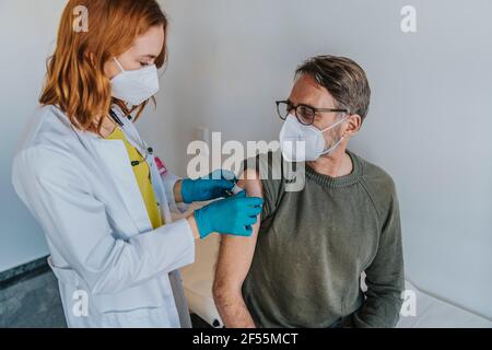 Expertise Tragen einer schützenden Gesichtsmaske, die einen Verband auf den Arm des Patienten legt Im Untersuchungsraum stehen Stockfoto