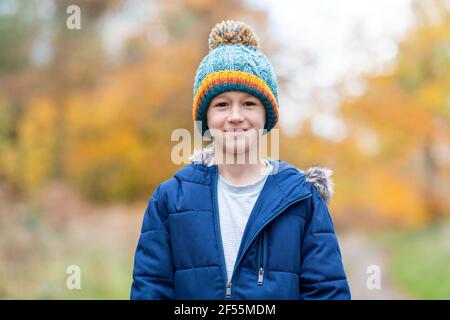 Junge in Strickmütze starrt, während er im Wald steht Stockfoto