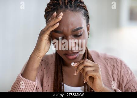 Verärgert schwarze Dame, die unter Kopfschmerzen oder Migräne zu Hause leidet, Pille nehmend Stockfoto