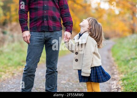 Lächelnde Tochter, die die Hand des Vaters hält, während sie im Wald steht Pfad Stockfoto